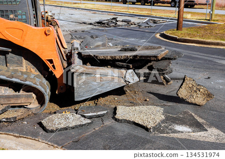 Skid steer removes asphalt pieces from city street for road repair work in parking lot Skid steer removes asphalt pieces from city street for road repair work in parking lot 134531974