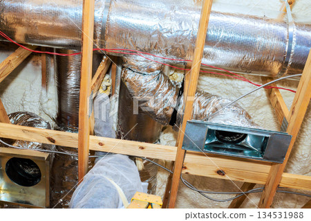 Workers are installing metal ducts in an attic, ensuring proper ventilation for new home. 134531988