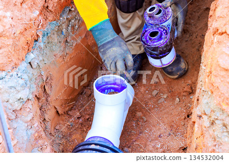 Worker applies purple primer to plastic pipes underground at construction site Worker applies purple primer to plastic pipes underground at construction site 134532004