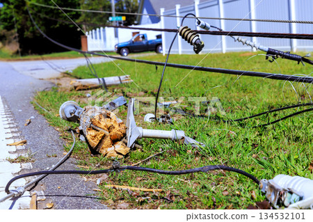 Power pole is down on grass with tangled wires scattered near road following hurricane storm in peaceful neighborhood. 134532101