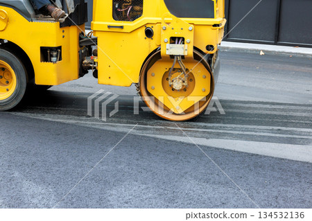 Heavy roller asphalt compactor compacts new asphalt on city street under smooth surface. 134532136