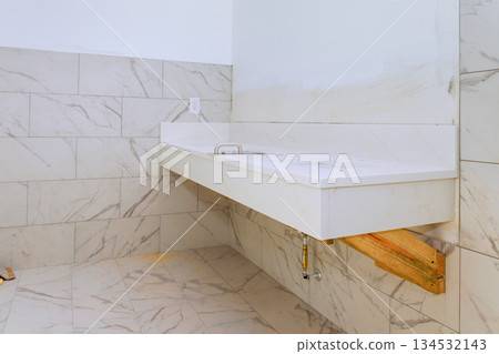 Open laundry space featuring clean white countertop above wooden support, surrounded by light marble tiles. Open laundry space featuring clean white countertop above wooden support, surrounded by light marble tiles. 134532143