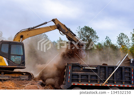 An excavator is actively transferring dirt into dump truck at construction site 134532150