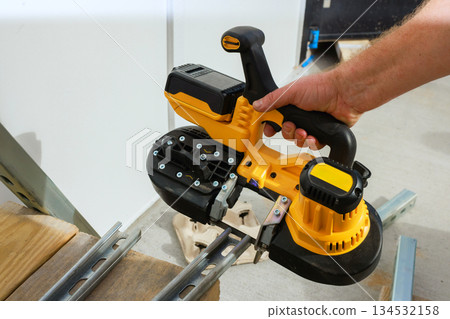 Skilled hands battery operated saw cutting metal framing at workshop Skilled hands battery operated saw cutting metal framing at workshop 134532158