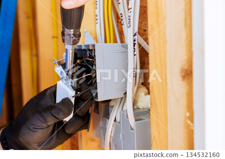 An electrician using screwdriver to connect wires inside an electrical panel in residential setting. An electrician using screwdriver to connect wires inside an electrical panel in residential setting. 134532160