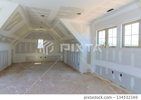 Spacious room with unfinished drywall bare floors, awaiting interior finishing touches in newly built house. 134532169