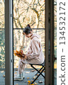 Woman sits on balcony holding bouquet of autumn leaves through open door. Restorative environments, connection with nature, slow living, mental wellbeing. 134532172
