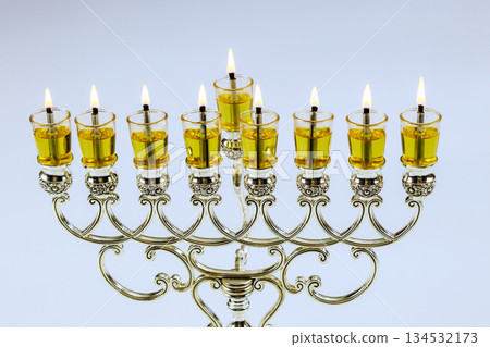 Menorah stands with glowing candles filled with oil, symbolizing holiday festival of lights during Hanukkah. Menorah stands with glowing candles filled with oil, symbolizing holiday festival of lights during Hanukkah. 134532173