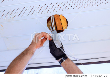 Electrician contractor is fitting light fixture into hole in ceiling while renovating their home Electrician contractor is fitting light fixture into hole in ceiling while renovating their home 134532177
