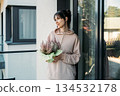 Woman holds potted heather plant on urban balcony. Urban sanctuary, mental restoration, residential wellness, greenery at home. 134532178