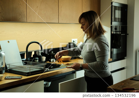 Woman stands in kitchen peeling carrot over sink. Zero waste lifestyle, organic waste, composting at home, sustainable living. Woman stands in kitchen peeling carrot over sink. Zero waste lifestyle, organic waste, composting at home, sustainable living. 134532196