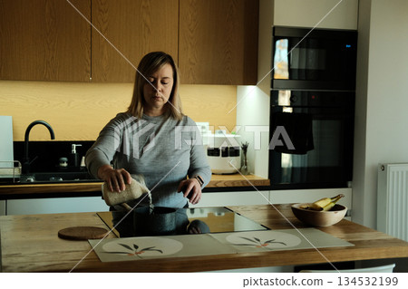 Woman stands in modern kitchen pouring rice from glass jar into pot on induction stove. Ergonomic workspace, high-end interior, smart home living, urban domesticity. Woman stands in modern kitchen pouring rice from glass jar into pot on induction stove. Ergonomic workspace, high-end interior, smart home living, urban domesticity. 134532199