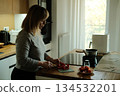 Woman slices red pepper on wooden countertop in modern kitchen. Compact living, modern kitchen design, studio apartment lifestyle. 134532201