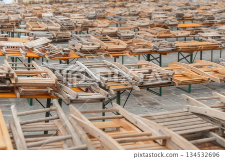 Wooden tables with stacked wooden chairs arranged in rows. Outdoor restaurant furniture prepared for storage or setup Wooden tables with stacked wooden chairs arranged in rows. Outdoor restaurant furniture prepared for storage or setup 134532696