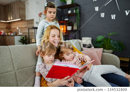 Mother looks at a book and reads a story to her daughters 134532809