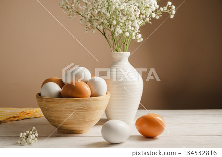 Easter eggs background. White eggs in wooden bowl and gypsophila flowers in a vase. Spring holiday Easter eggs background. White eggs in wooden bowl and gypsophila flowers in a vase. Spring holiday 134532816