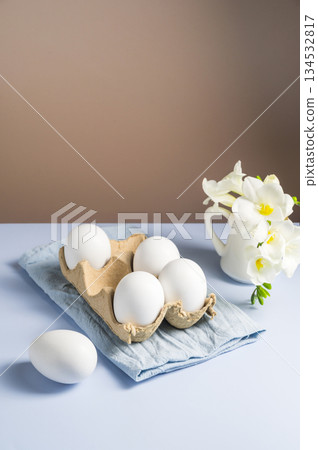 Easter eggs and flowers. White eggs in cardboard box and Freesia white spring bouquet in a ceramic jug 134532817