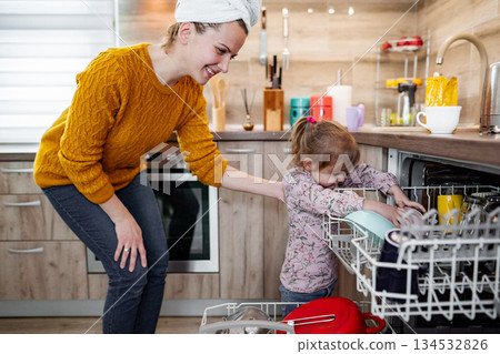 Little girl helping her mum load the dishwasher in the kitchen 134532826