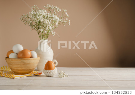 Easter eggs background. White eggs in wooden bowl and gypsophila flowers in a vase. Spring holiday Easter eggs background. White eggs in wooden bowl and gypsophila flowers in a vase. Spring holiday 134532833