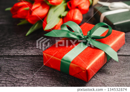 Red gift box with ribbon and fresh red tulip flowers. Easter or birthday holiday black background. Red gift box with ribbon and fresh red tulip flowers. Easter or birthday holiday black background. 134532874