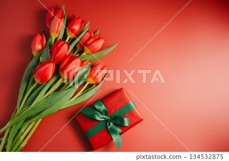 Celebration background. Mothers' day. Red tulips with a gift box. Red background, copy space. Celebration background. Mothers' day. Red tulips with a gift box. Red background, copy space. 134532875