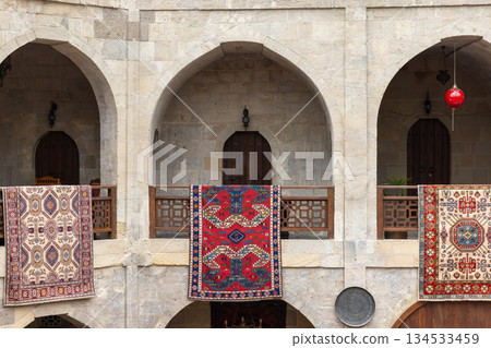 Historic stone arches frame a sunny courtyard, with vibrant Persian rugs 134533459