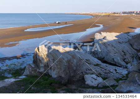 A serene coastal landscape featuring large rocks in shadow and sandy shoreline A serene coastal landscape featuring large rocks in shadow and sandy shoreline 134533464