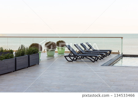 Relaxing poolside scene with sleek black loungers facing the calm sea Relaxing poolside scene with sleek black loungers facing the calm sea 134533466