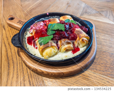 Warm skillet of homemade crepes swirled in ruby-red berry sauce and adorned with fresh mint for an elegant breakfast spread Warm skillet of homemade crepes swirled in ruby-red berry sauce and adorned with fresh mint for an elegant breakfast spread 134534225