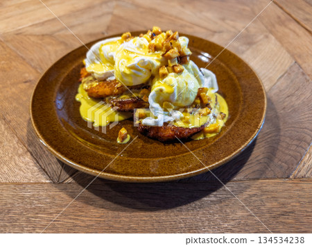 Gourmet breakfast presentation of crisp hash brown cakes layered under silky poached eggs drizzled with hollandaise 134534238
