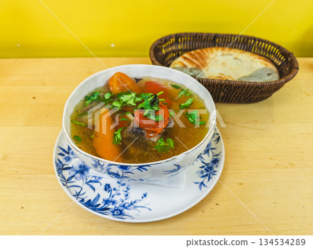 Uzbek shurpa soup with lamb carrots cilantro and flatbread on wood table before yellow wall 134534289
