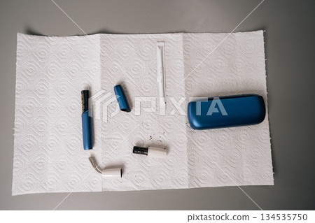 Top view of disassembled electronic cigarette parts placed on absorbent paper during cleaning and maintenance process, using cleaning stick for thorough hygiene, no people, nobody, close-up. 134535750