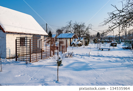Snowy Winter Garden with Bench and Small Houses at Sunrise 134535964