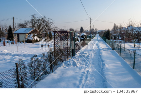Snowy Winter Garden with Bench and Small Houses at Sunrise Snowy Winter Garden with Bench and Small Houses at Sunrise 134535967