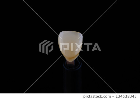 Close up shot ultra thin dental zirconium crown is held with tweezers with black background. 134538345
