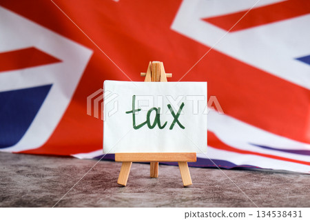 Paper note with words TAX on National symbol of Great Britain. British wave the UK silky flag background. Tax planning system and economy policy Paper note with words TAX on National symbol of Great Britain. British wave the UK silky flag background. Tax planning system and economy policy 134538431