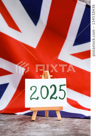 Paper note with text 2025 on National symbol of Great Britain. British wave the UK silky flag background. Financial outlook planning, new year annual report Paper note with text 2025 on National symbol of Great Britain. British wave the UK silky flag background. Financial outlook planning, new year annual report 134538436