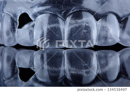 Printed transparent dental cap made of polymer on a light colorful background. Dental splint against bruxism. Printed transparent dental cap made of polymer on a light colorful background. Dental splint against bruxism. 134538497