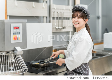女廚師正在瓦斯爐上的煎鍋裡烹飪。 女廚師正在瓦斯爐上的煎鍋裡烹飪。 134539430
