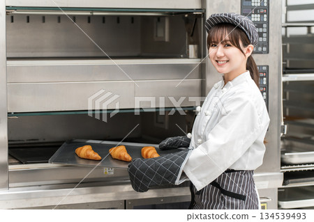 一名女廚房工作人員正在從烤箱裡取出麵包和羊角麵包。 134539493