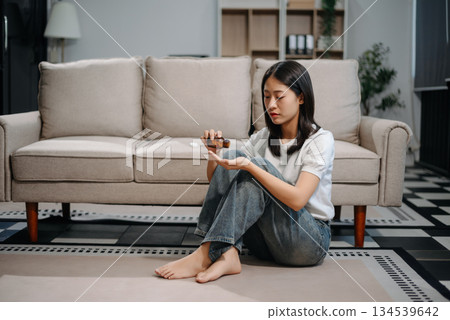 Asian woman sit Depression Dark haired  pensive glance Standing by window and anxiety Copy space with a blanket on a sofa. 134539642