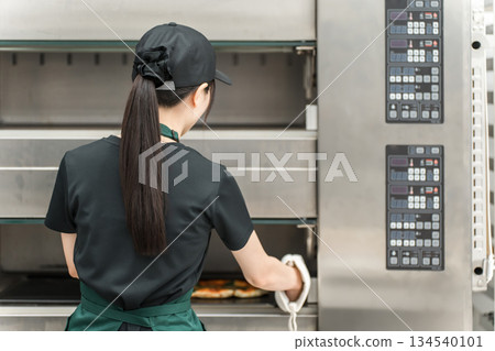 Female chef taking pizza out of the oven Female chef taking pizza out of the oven 134540101