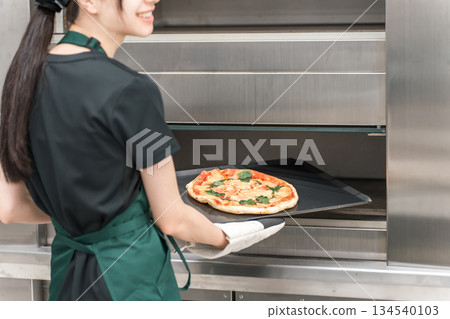 Female chef taking pizza out of the oven Female chef taking pizza out of the oven 134540103