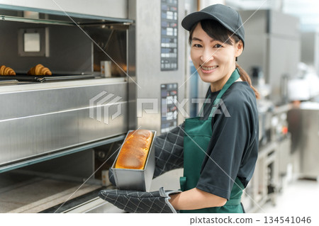 A female kitchen staff member taking bread out of the oven 134541046