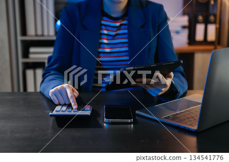 Women counting coins on calculator taking from the piggy bank. hand holding pen working on calculator at home office. 134541776