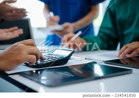 Medical team having a meeting with doctors in white lab coats and surgical scrubs seated at a table discussing a patients working online using computers Medical team having a meeting with doctors in white lab coats and surgical scrubs seated at a table discussing a patients working online using computers 134541850
