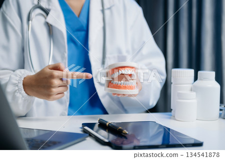 Dentist sitting at table with jaw samples tooth model and working with tablet and laptop in dental modern office Dentist sitting at table with jaw samples tooth model and working with tablet and laptop in dental modern office 134541878