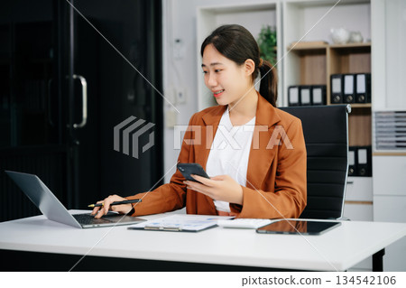 Asian woman using laptop and tablet while sitting at her working place. Asian woman using laptop and tablet while sitting at her working place. 134542106