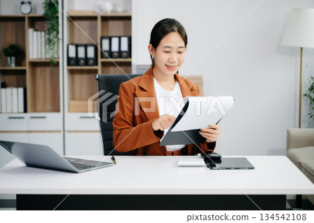 Asian woman using laptop and tablet while sitting at her working place. 134542108