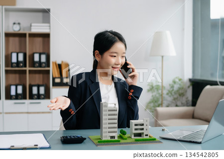 Young real estate agent worker working with laptop and tablet at table in office and small house beside it. 134542805